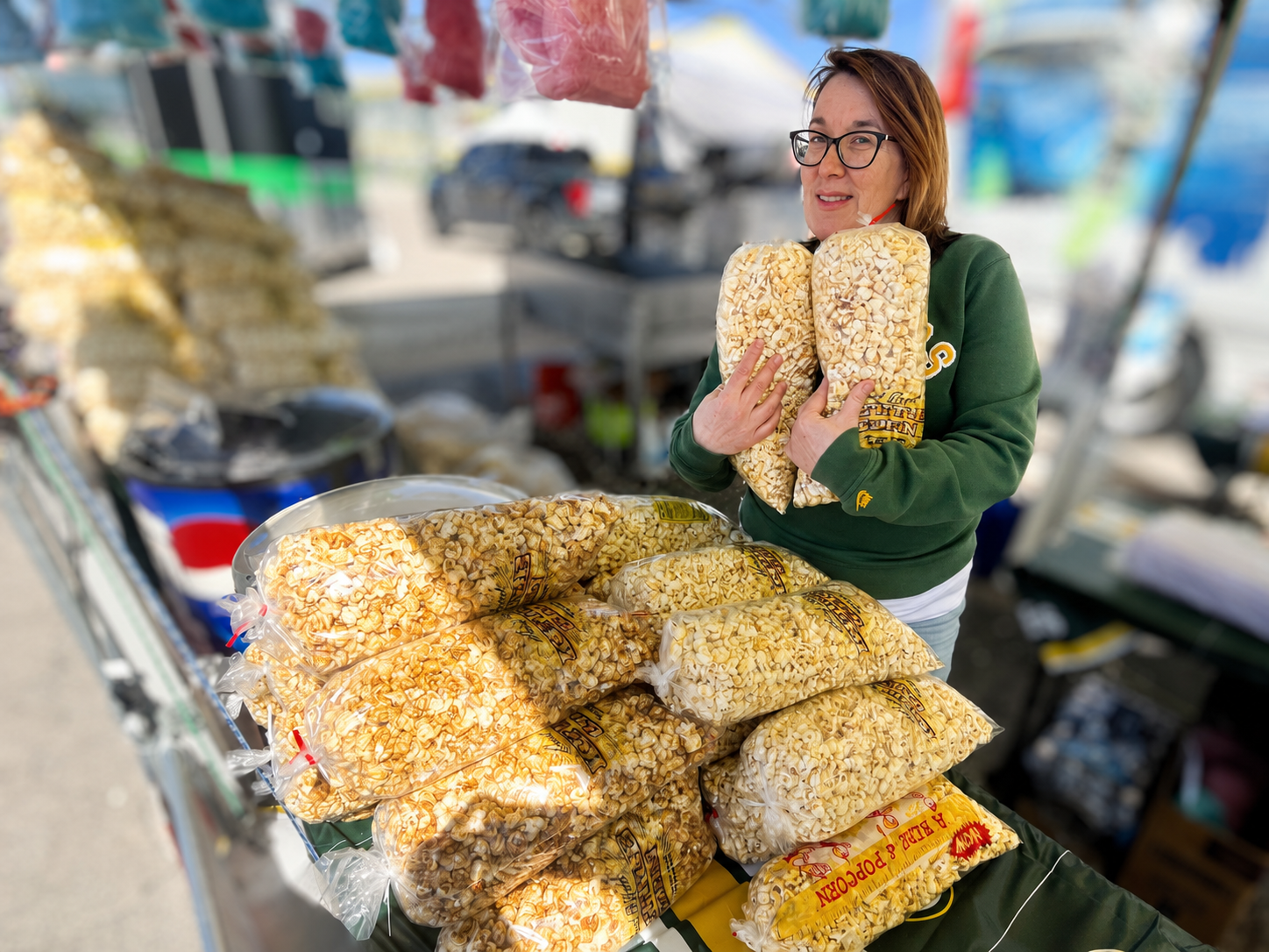 Fun Fest Foods kettle corn vendor holding bags of fresh kettle corn with stacked popcorn bags at an event stand